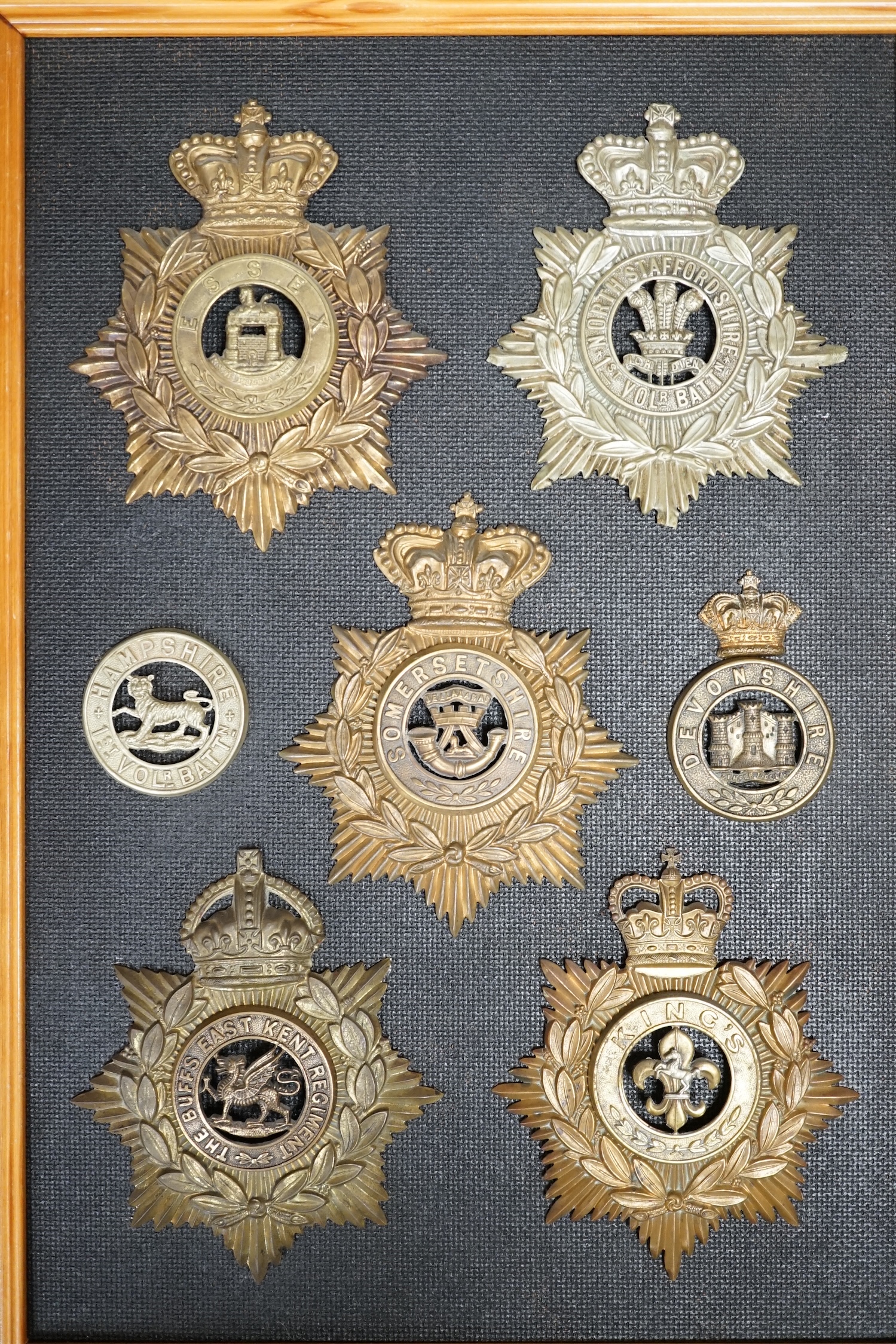 Five military helmet plates and two other centre badges, mounted on a board including; the Essex Regiment, the North Staffordshire 1st Volunteer Battalion, the Somerset Regiment, the Buffs East Kent Regiment, the King’s